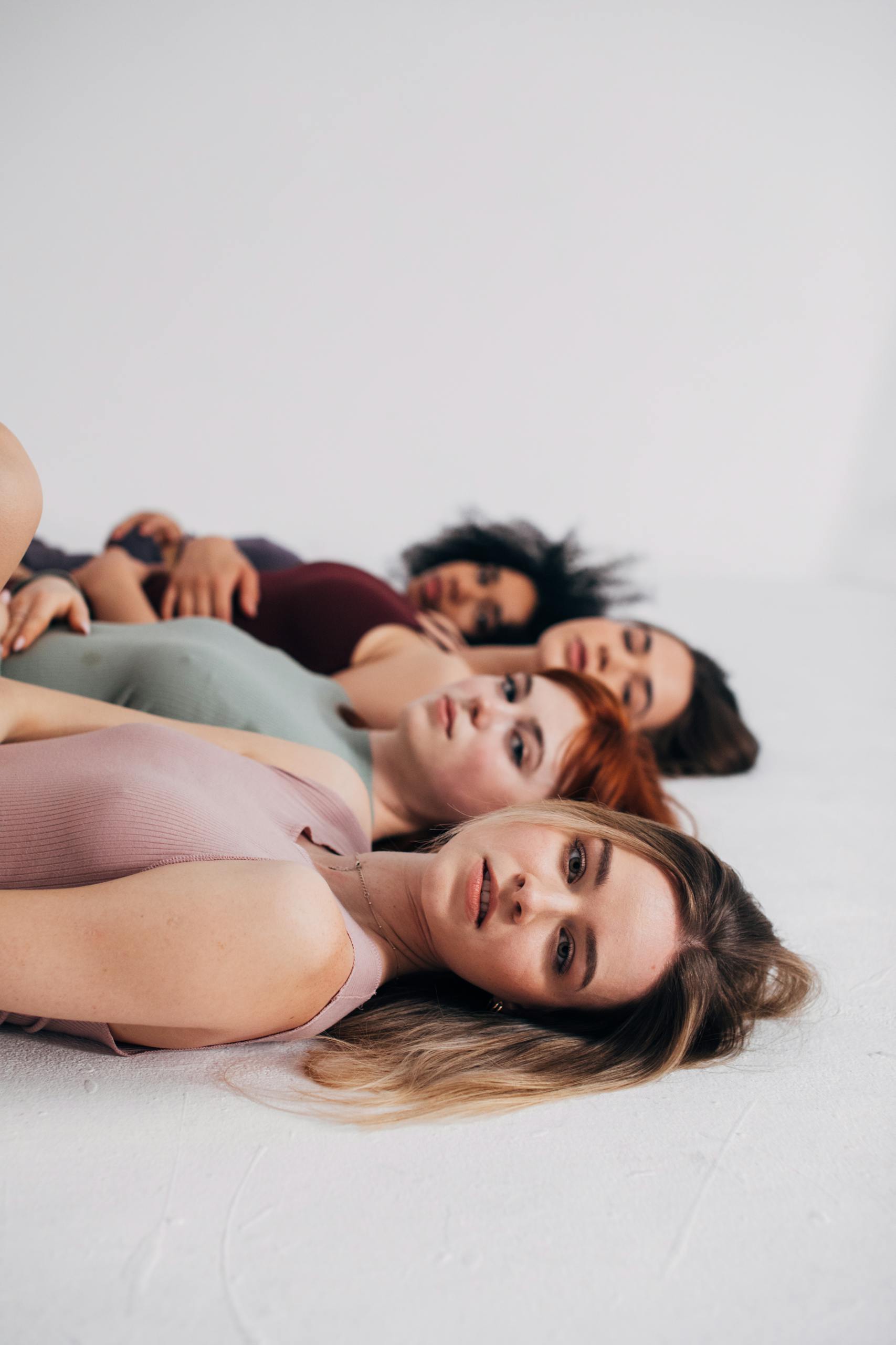 Portrait of diverse women in casual wear lying down in a studio setting, showcasing beauty and diversity.